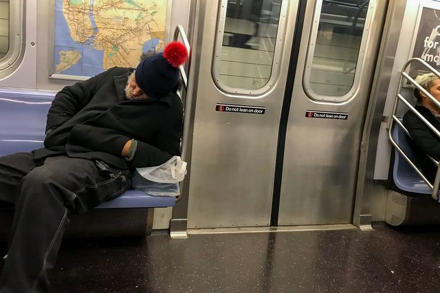 A homeless man sleeps on a subway train car.